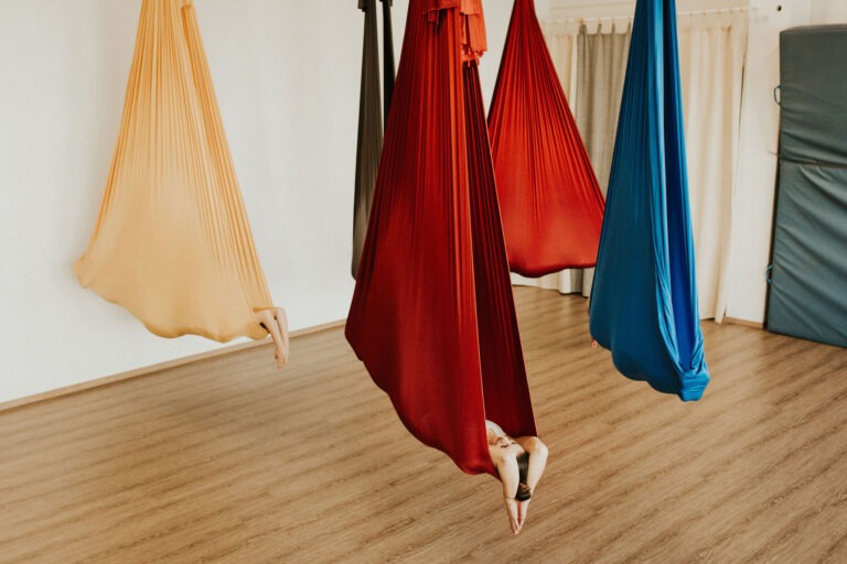 Eine Person liegt bei Aerial Yoga auf dem Bauch im Tuch, mit ausgestreckten Armen und Beinen, während der Körper sanft im Tuch schwebt.